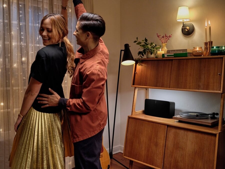 A couple dancing together in a room with a Sonos system’s speaker on a table next to them.